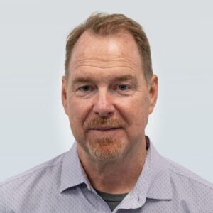 Tom Barron's headshot, wearing grey button up