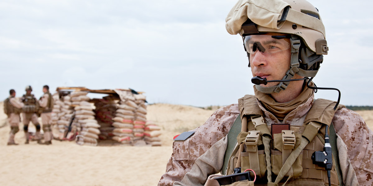 US military service member standing in a desert using a headset for communication.