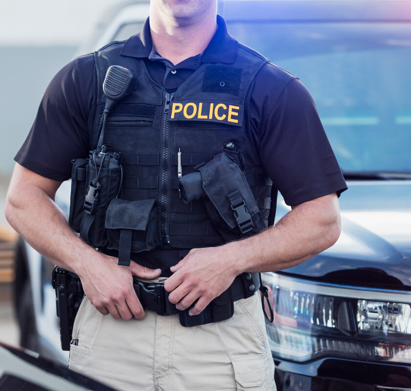A police office in uniform standing in front of a police car.