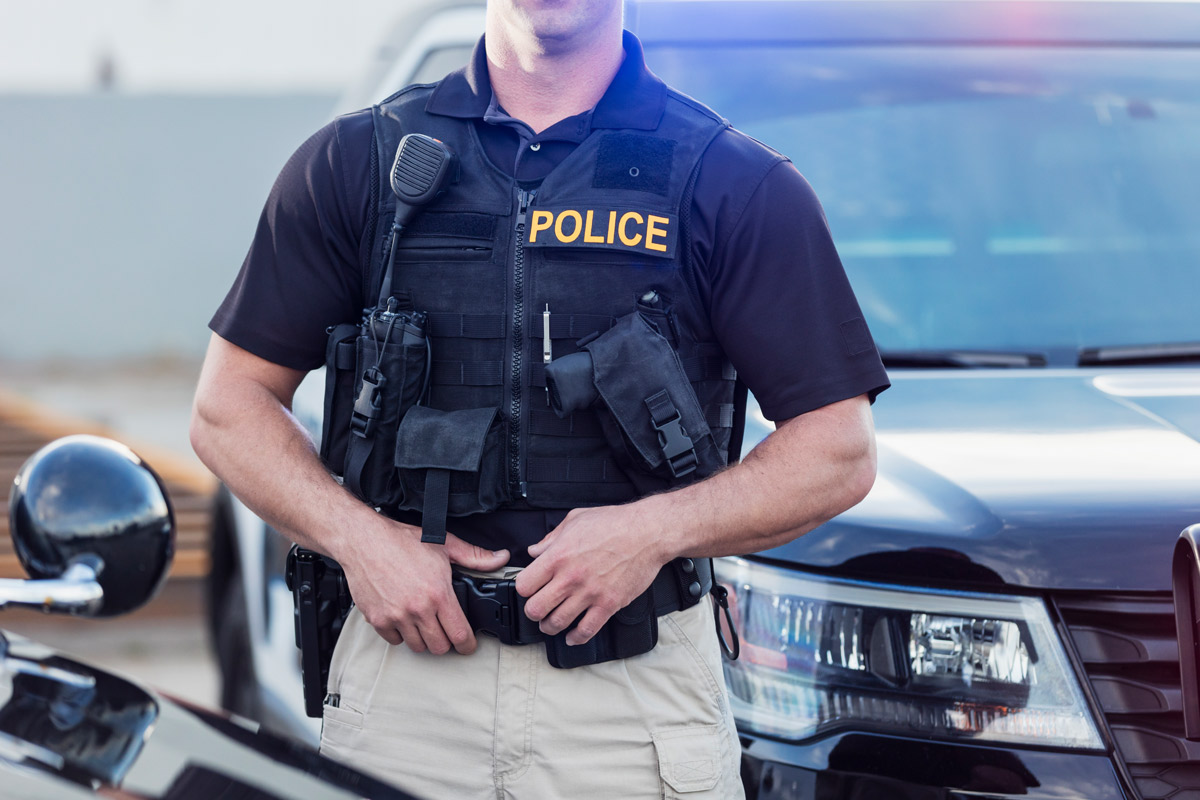 A police office in uniform standing in front of a police car.
