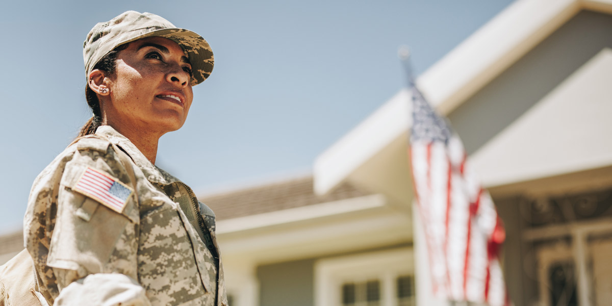 A US military service member with American flag flying in the background.